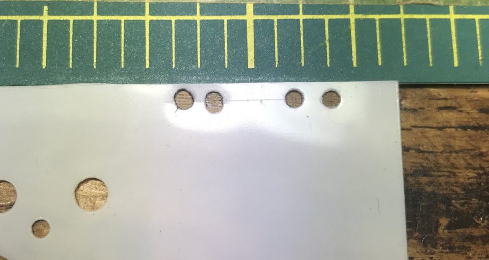 The stencil plastic template: two pairs of holes, the left pair slightly closer together than the right.