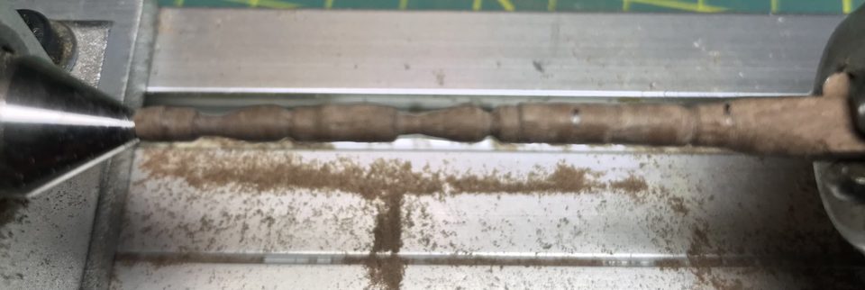 A stanchion taking shape between the centres of the lathe; the curves are already started.