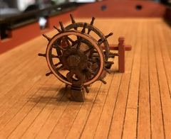 The ship's wheel with copper rim band, trial-fitted on deck next to the bitts