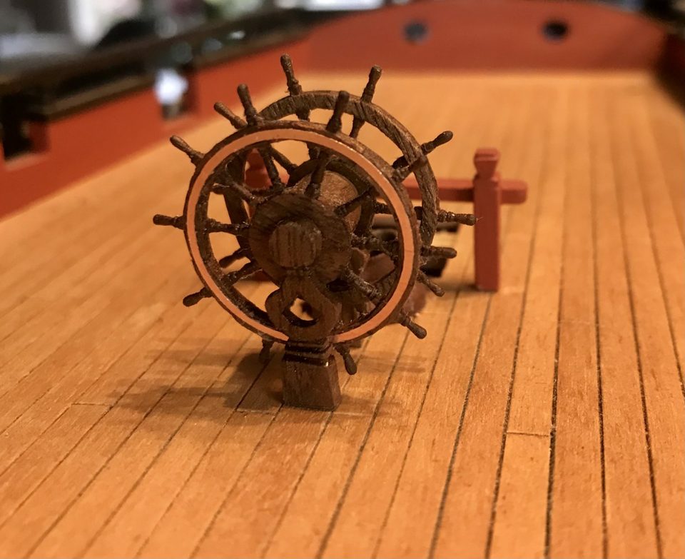 The ship's wheel with copper rim band, trial-fitted on deck next to the bitts