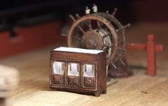 The first side of the binnacle with walnut stain, trial-fitted in front of the ship's wheel